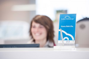 Mitarbeiterin hinter Service-Tisch mit kundenfreundlichem Schild "Ganz.Nah.Da". Feigfotodesign
