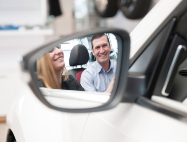 Mitarbeiter erklärt Kundin Auto, Blick über Rückspiegel. Feigfotodesign
