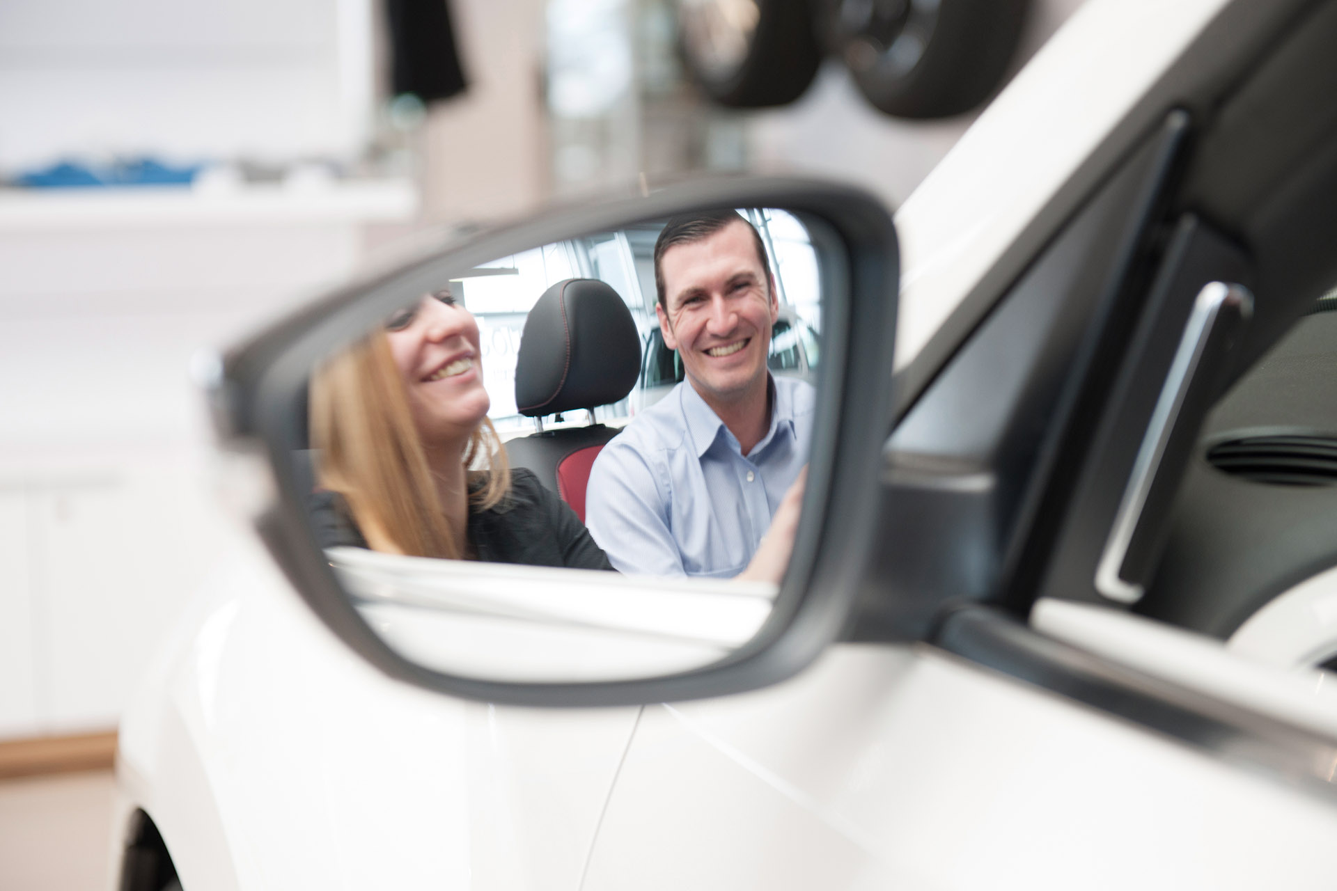 Mitarbeiter erklärt Kundin Auto, Blick über Rückspiegel. Feigfotodesign