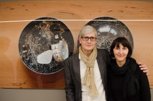 Fotografen Alexander und Antonia Feig vor Bild mit Stecknadeltöpfchen und Maßband. Feigefotodesign