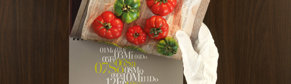 Hand mit Handschuh blättert im Kalender zu Monat Juli mit Tomaten-Motiv. Feigefotodesign
