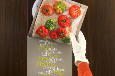 Hand mit Handschuh blättert im Kalender zu Monat Juli mit Tomaten-Motiv. Feigefotodesign